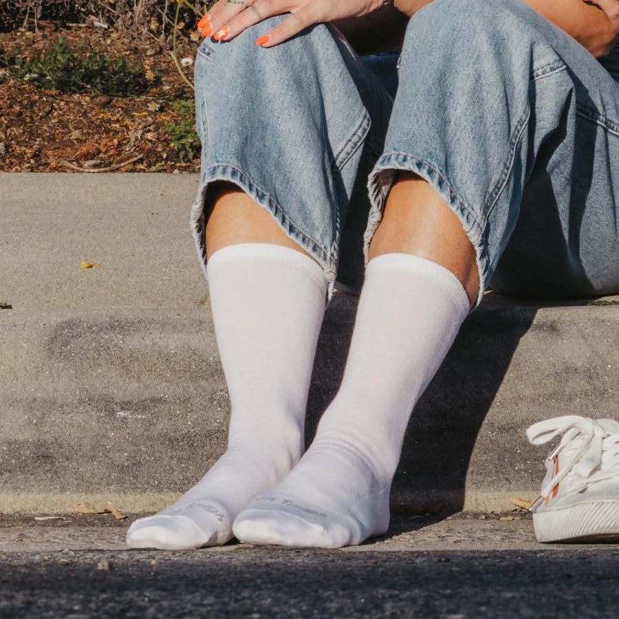 Person wearing white knee-high socks and blue jeans sitting on a concrete step.