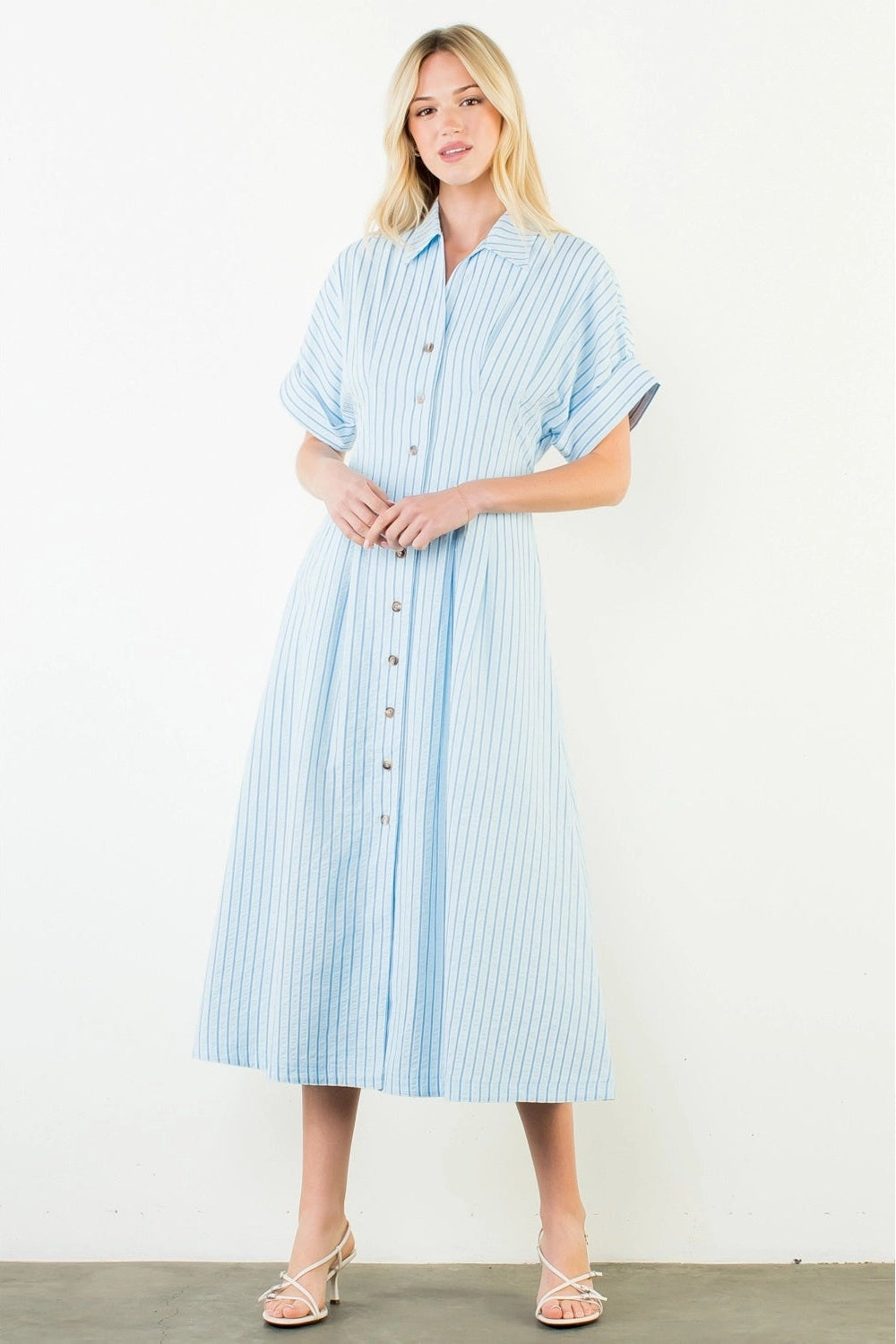 Woman wearing a light blue and white striped dress against a plain background