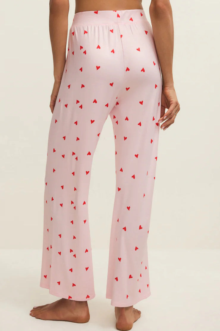 Pink pajama pants with red heart pattern worn by a person on a white background