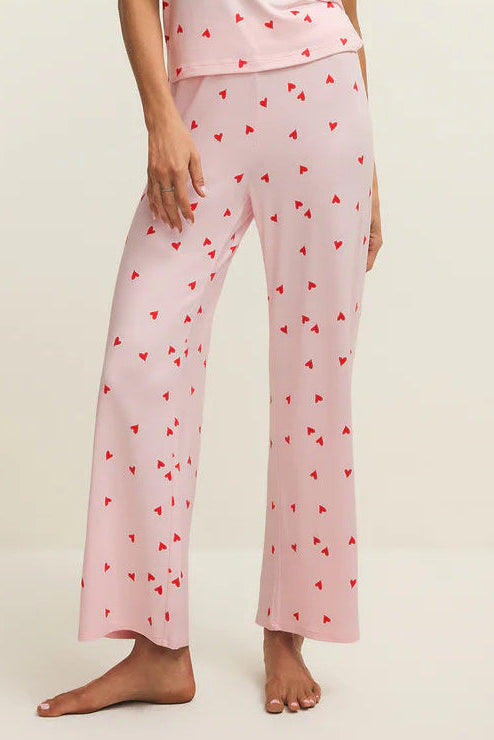 Woman wearing a pink pajama set with heart patterns on a beige background