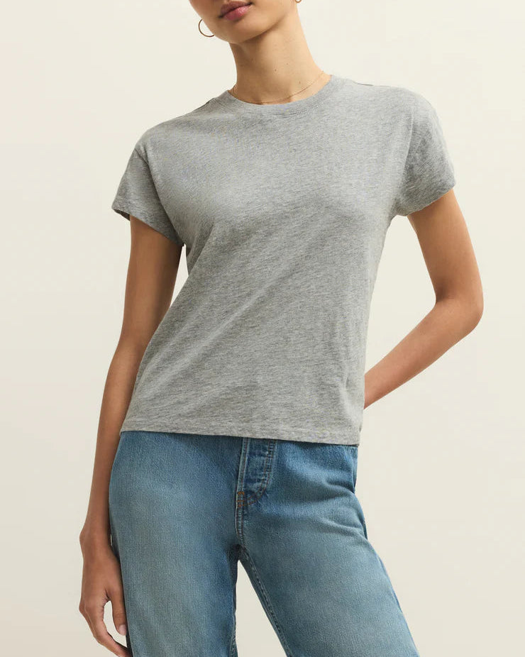 Woman wearing a gray t-shirt and blue jeans against a beige background