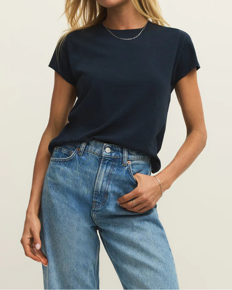 Woman wearing a navy t-shirt and blue jeans against a plain background