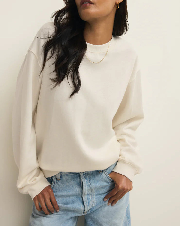 Woman wearing a white sweatshirt and light blue jeans against a plain background