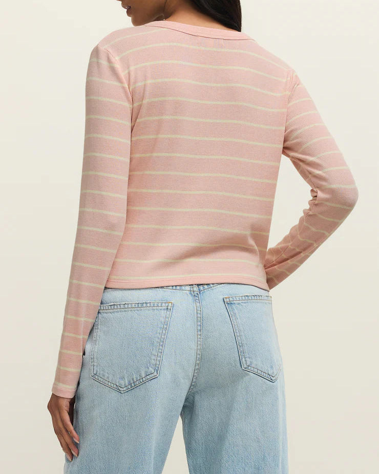 Woman wearing a pink striped long-sleeve top and light blue jeans on a beige background