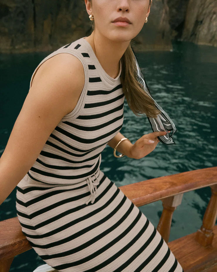 Woman in a striped dress sitting by a body of water with rocky cliffs in the background
