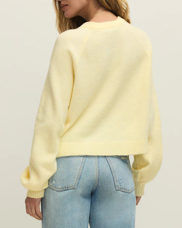 Woman wearing a light yellow sweater and blue jeans against a plain background