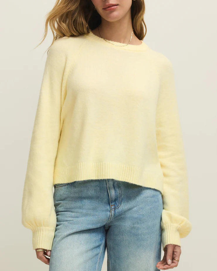 Woman wearing a light yellow sweater and blue jeans against a plain background