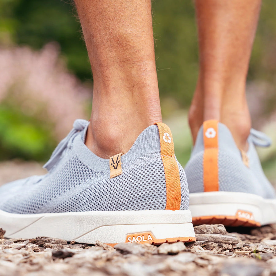 Person wearing blue athletic shoes with orange accents on a natural background