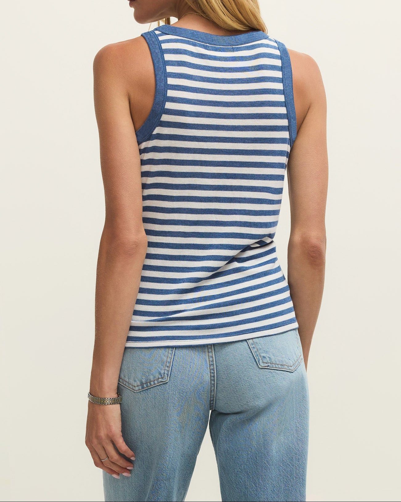 Woman wearing a blue and white striped tank top and light blue jeans on a plain background