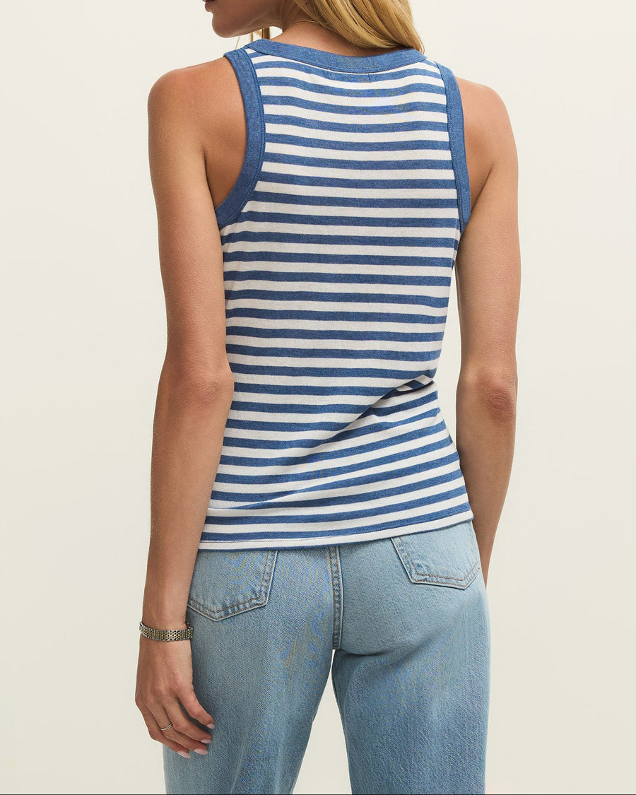 Woman wearing a blue and white striped tank top and light blue jeans on a plain background