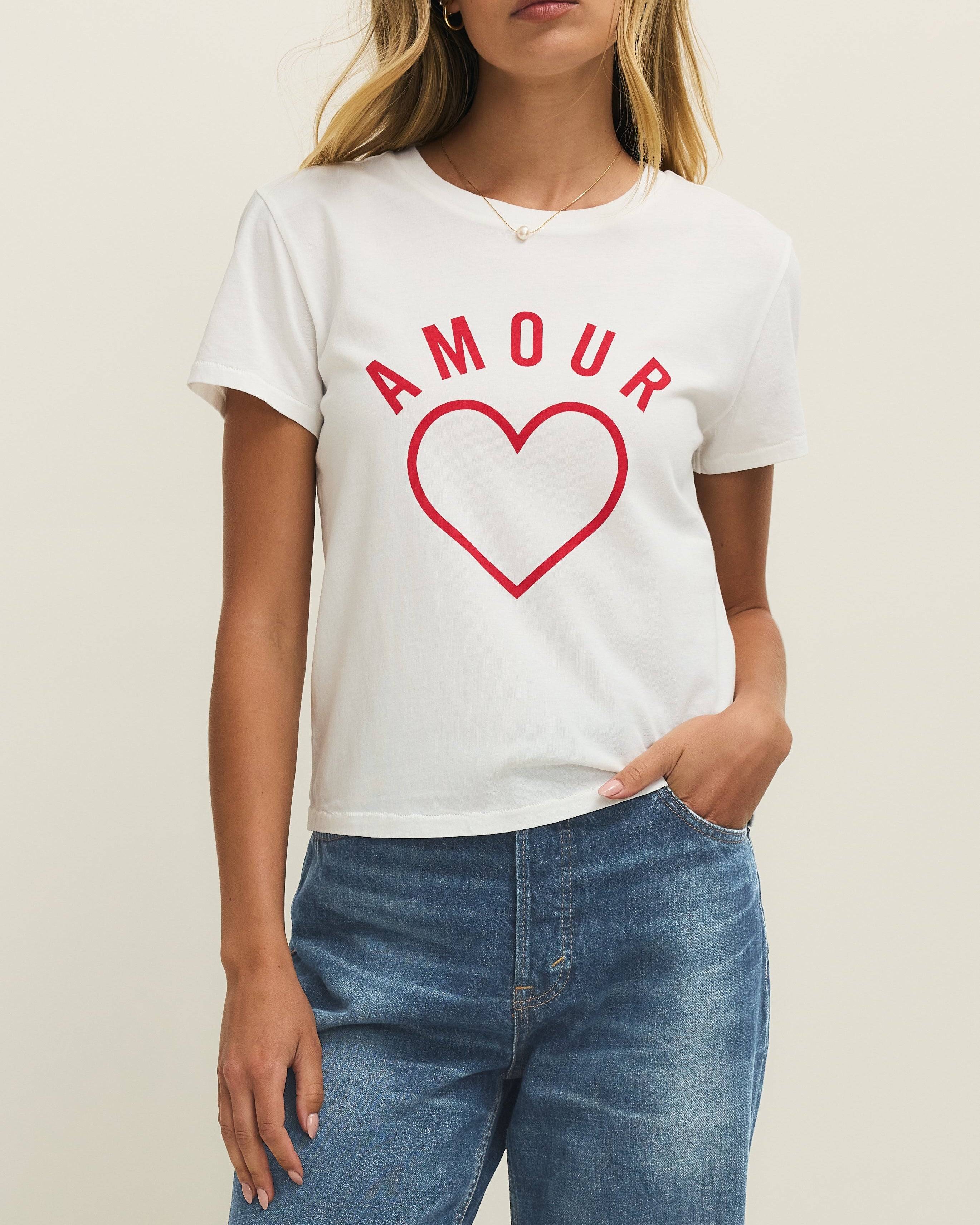 Woman wearing a white t-shirt with 'AMOUR' and a red heart design, standing against a plain background.