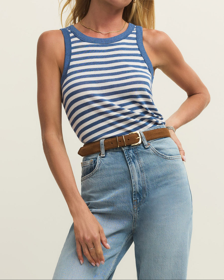 Woman wearing a blue and white striped tank top and light blue jeans against a plain background
