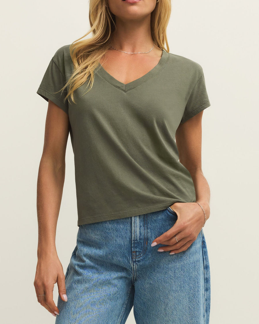 Woman wearing an olive green t-shirt and blue jeans against a plain background