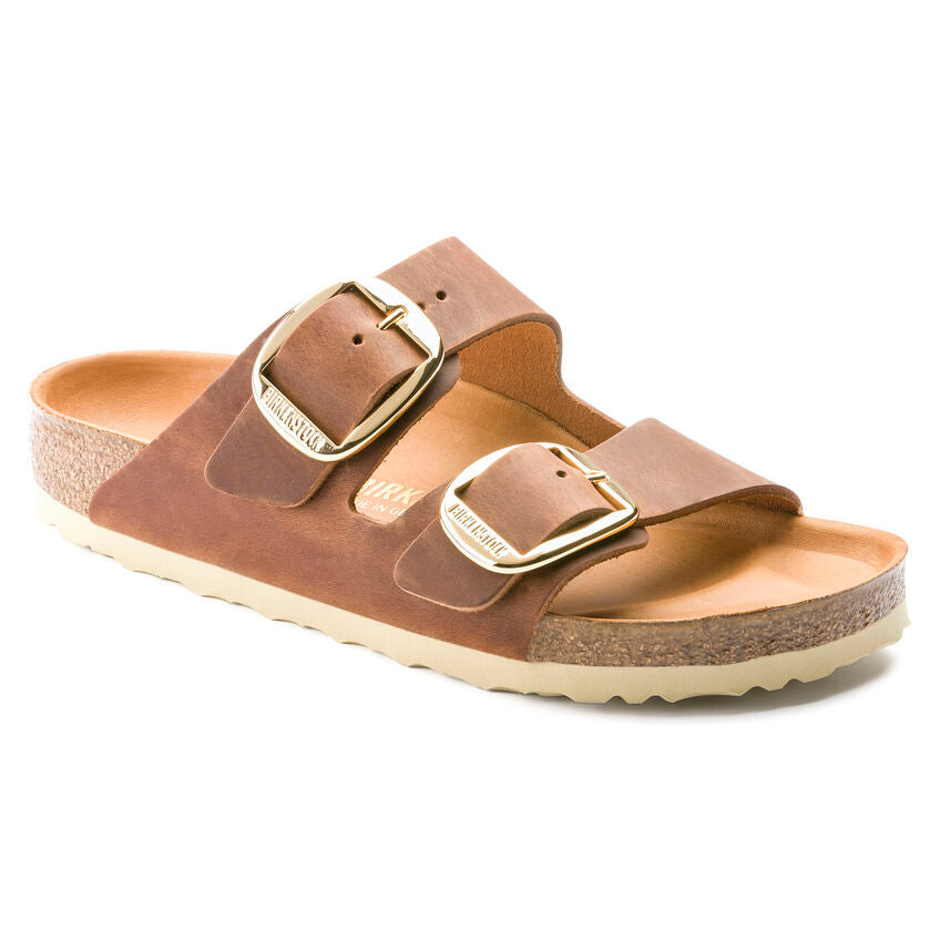 A person wearing Birkenstock Arizona sandals with a big buckle, in a beige color, on a white background.